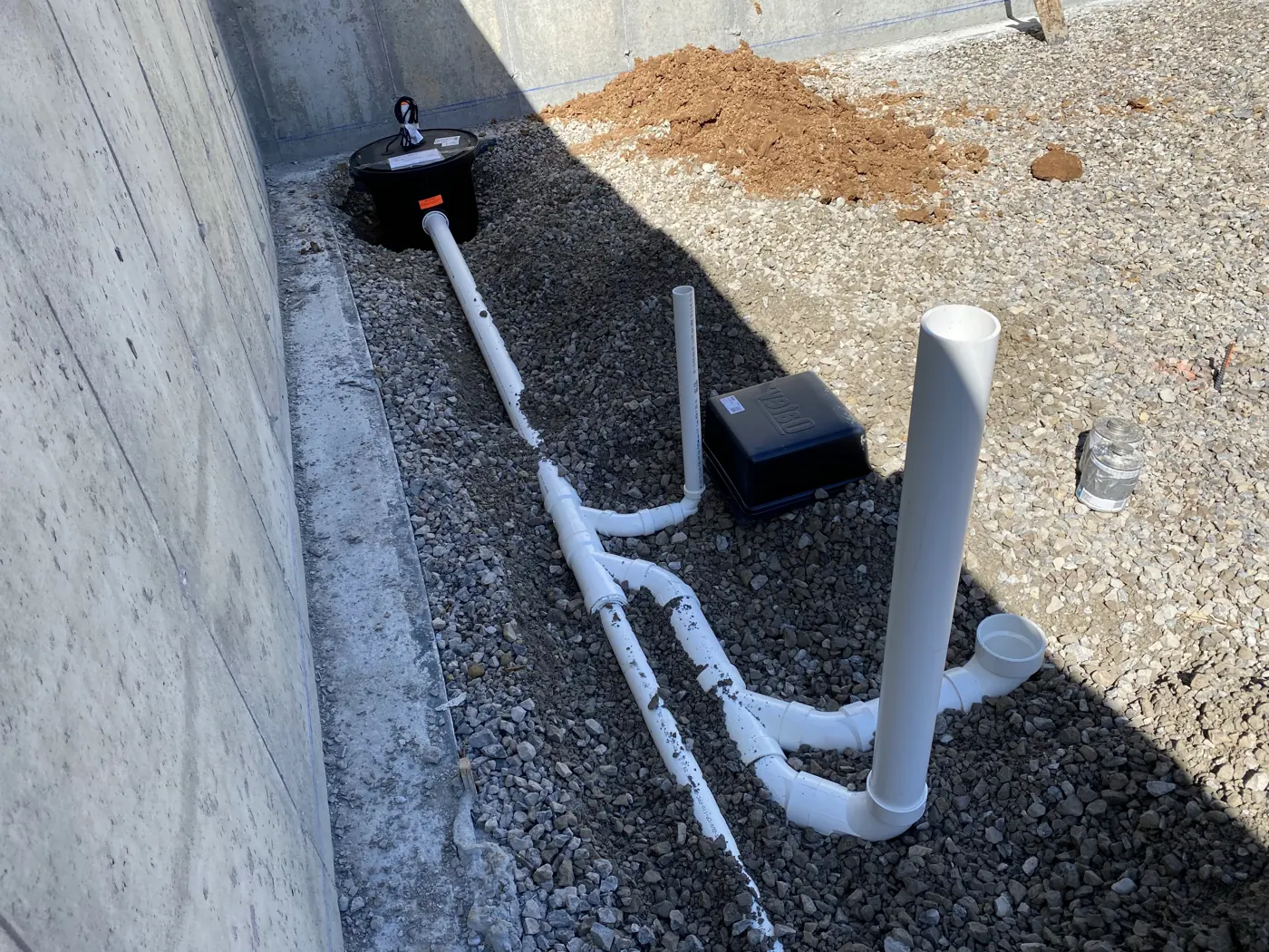 White PVC drain piping laid in gravel beside a concrete foundation wall