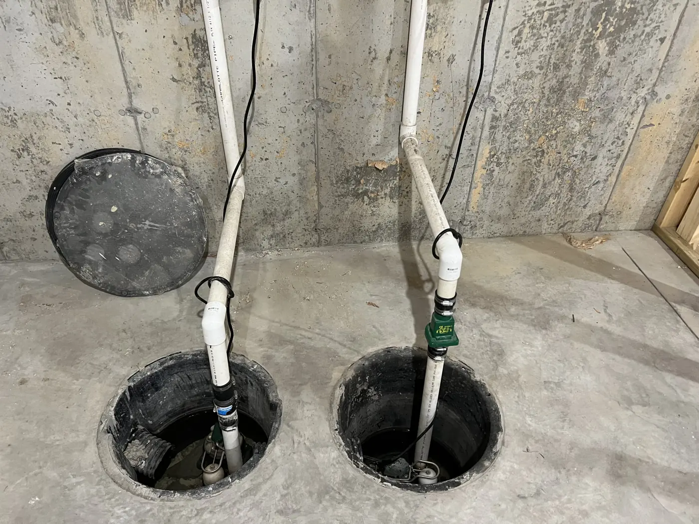 Two sump-pump pits with pumps and white discharge pipes in a concrete basement floor